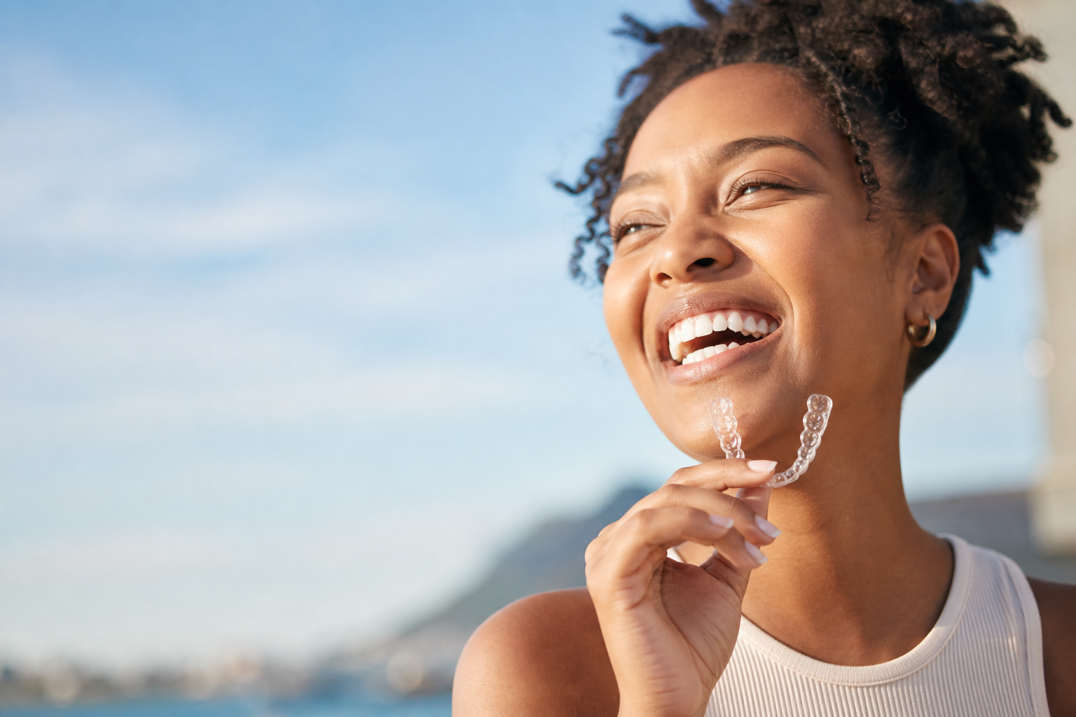 Smiling South African woman holding her clear aligner